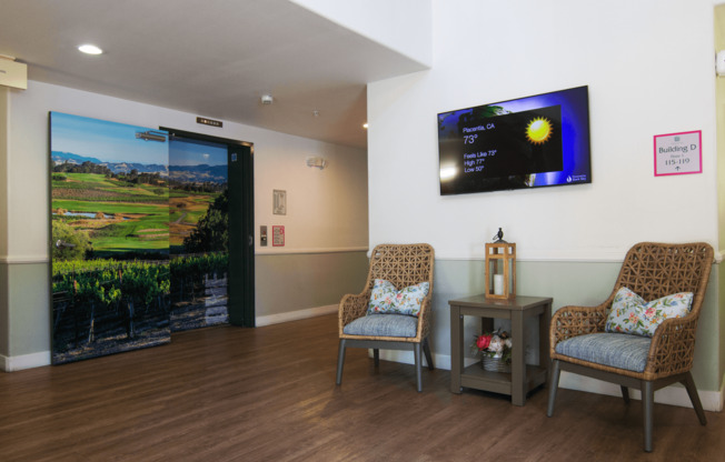 A room with a television on the wall and two chairs in front of it.