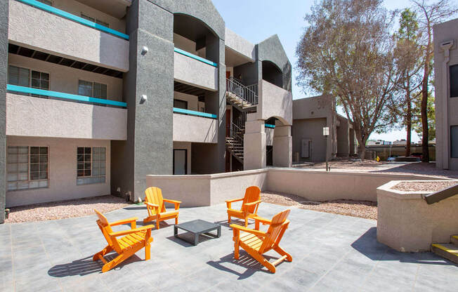 Four orange chairs are placed on a patio in front of a building.