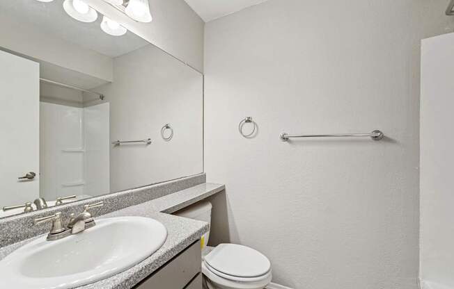A bathroom with a toilet, sink, mirror, and towel rack.