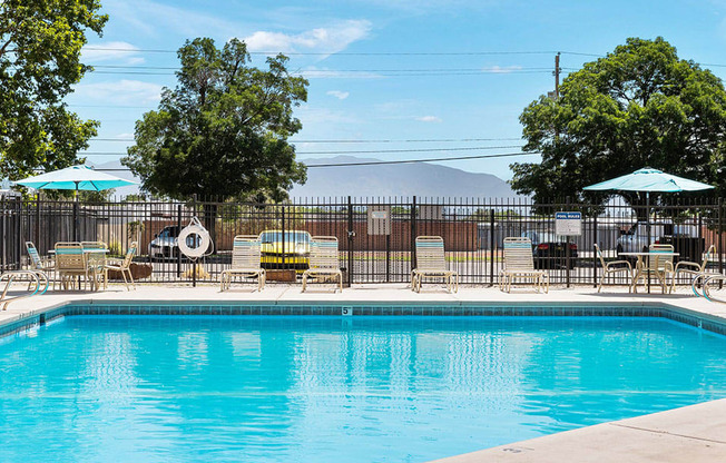 a swimming pool with chairs and umbrellas and trees in the background