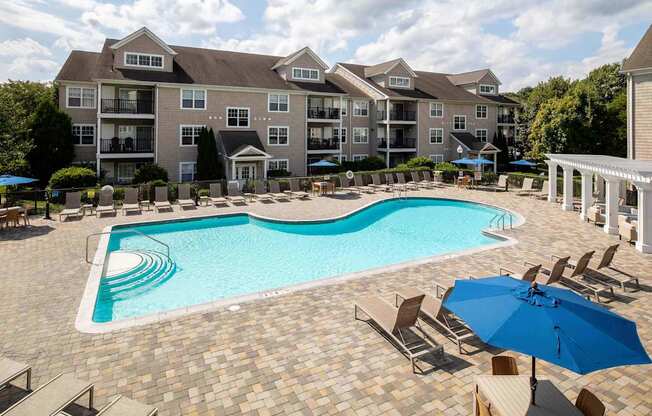 a swimming pool with chairs and umbrellas in front of an apartment building