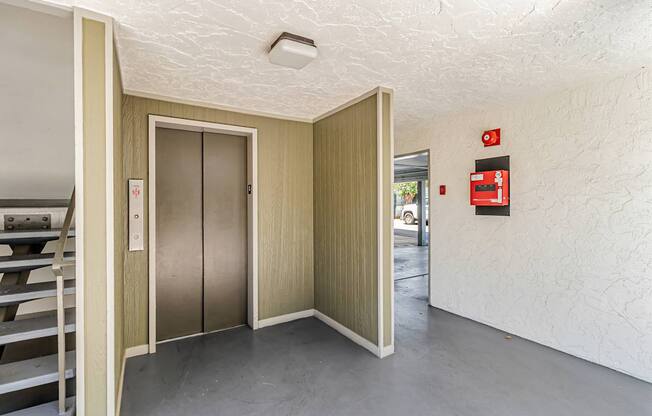 A room with a white ceiling and a grey floor with a wooden door and a red fire extinguisher on the wall.
