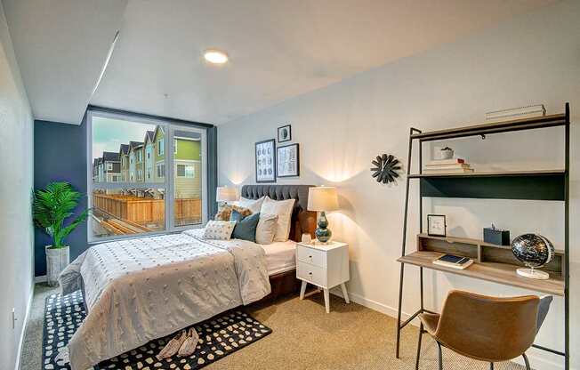 One Bedroom Apartments in West Seattle WA - Upton Flats - Spacious Bedroom wtih Carpetted Floor, Bed, Nightstands with Lamps, Desk, Large Window, and House Plant