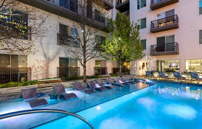 A swimming pool with lounge chairs and apartment buildings in the background.