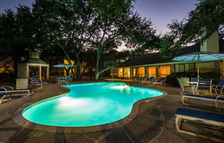 a night view of a pool with lounge chairs and umbrellas