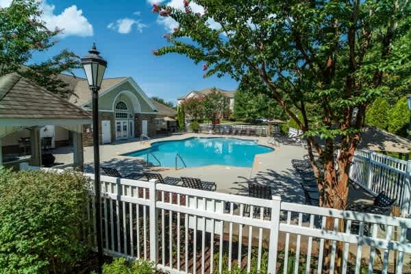 A pool surrounded by a white fence and trees.