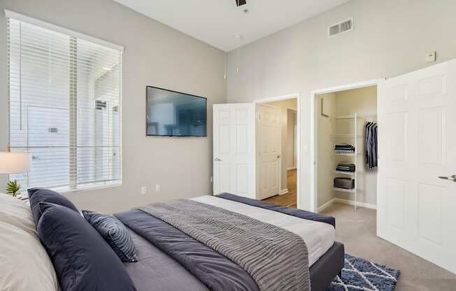 A bedroom with a bed, a window with blinds, a ceiling fan, and a closet with clothes.