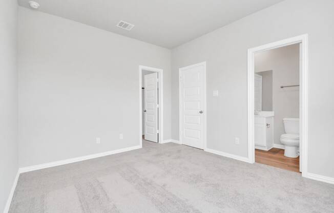 a bedroom with two doors and a bathroom in the background