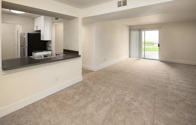 A spacious living room with a kitchenette and sliding glass doors leading to a balcony.