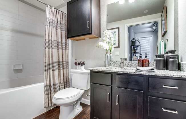 A white toilet sits in a bathroom with a black cabinet and a white bathtub.