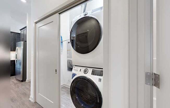 a white and black stackable full-size washer and dryer in a double door closet in the front hallway