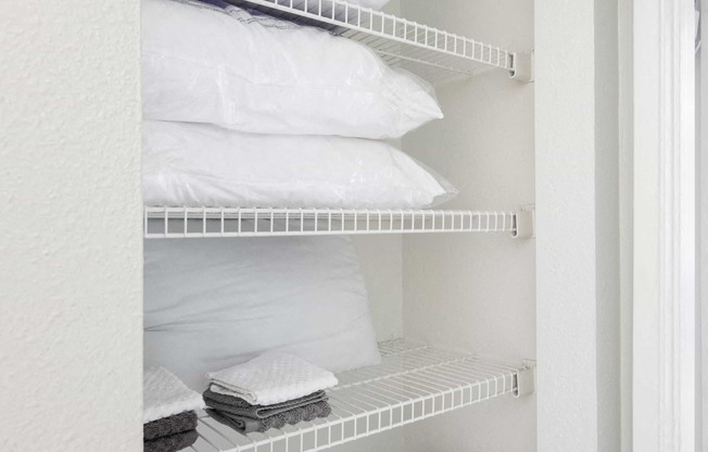 a white closet with shelves filled with folded white towels and pillows