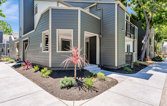 A modern house with a grey exterior and a small garden in front.