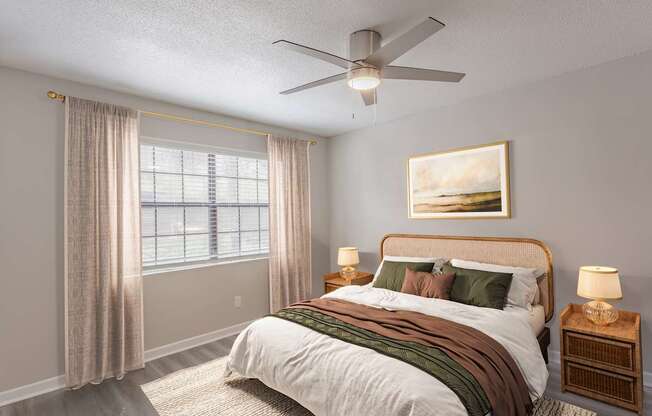 A bedroom with a large bed, a ceiling fan, and a painting on the wall.