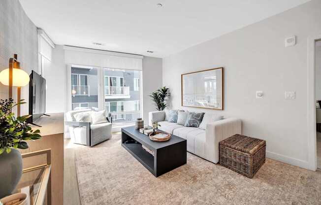 A living room with a white couch, a coffee table, and a large window.