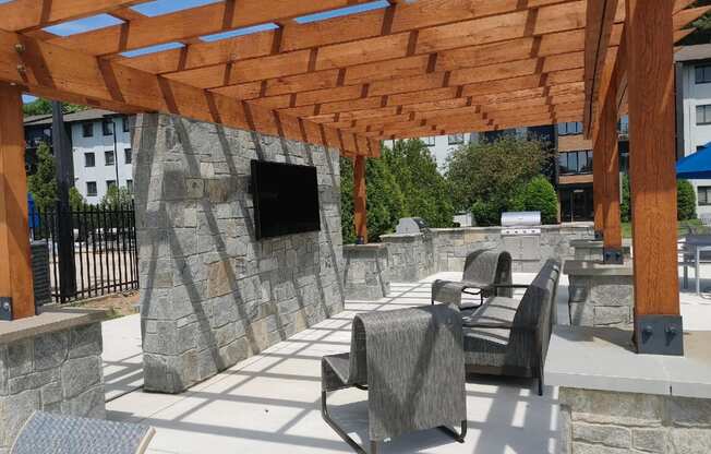 Outdoor pergola with chairs and a tv on a stone wall at  Woods of Fairfax