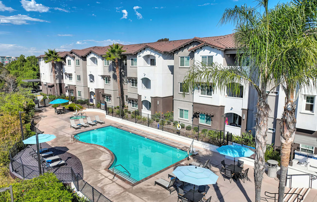 A large swimming pool surrounded by chairs and umbrellas in front of apartment buildings.