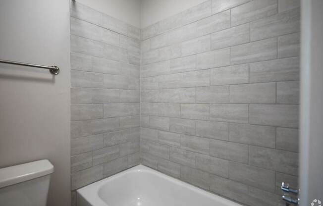 A white bathtub sits in a bathroom with a grey tiled wall.
