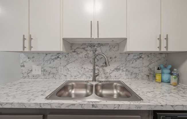 a kitchen sink with marble counter top and white cabinets