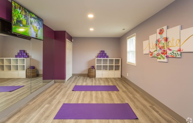 a yoga room with purple yoga mats and a tv