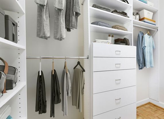 A white closet with clothes and shoes.