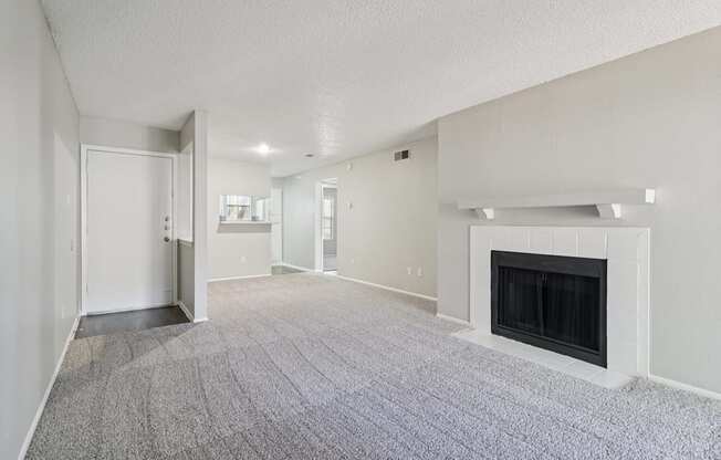 A spacious living room with a fireplace and grey carpeting.