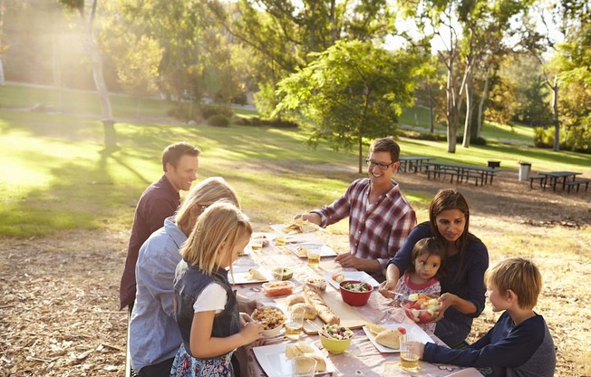 a group of people sitting around a table eating food in a park