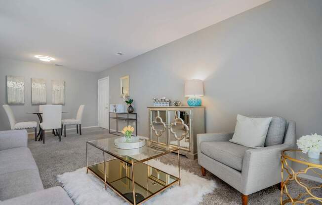 A modern living room with a glass coffee table and grey couches.