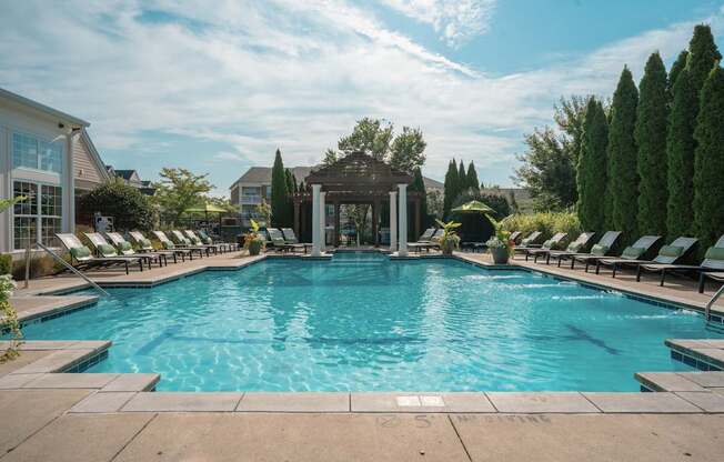 A large outdoor swimming pool surrounded by lounge chairs and trees.