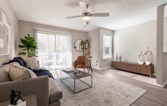 A living room with a grey couch, a glass coffee table, and a ceiling fan.
