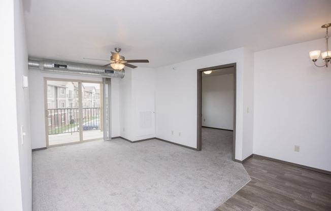 an empty living room with a ceiling fan and a door to a balcony