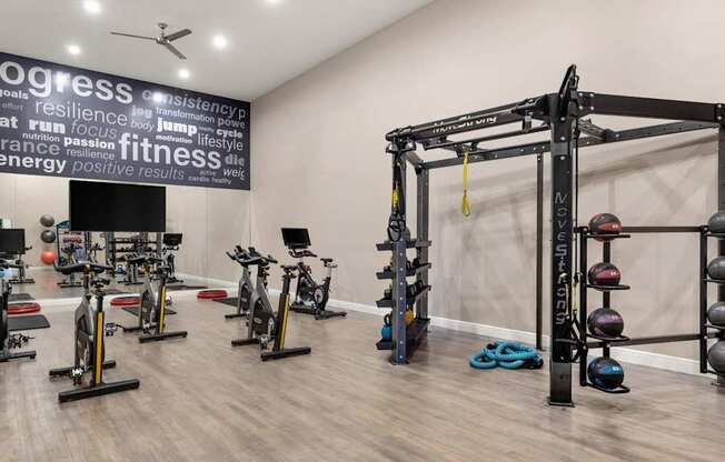 A gym with a variety of equipment including a squat rack, dumbbells, and exercise bikes.