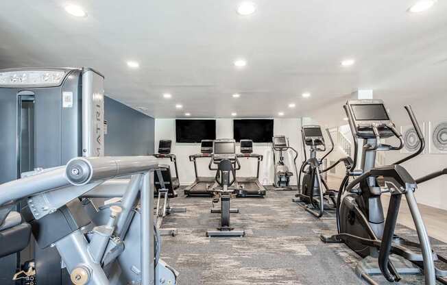 A gym with a variety of exercise equipment including treadmills, stationary bikes, and weight machines.