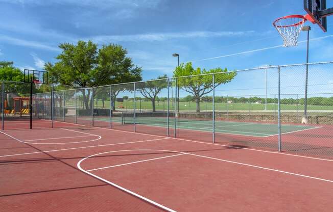 Sports court with basketball hoops and tennis court in the back at Chisholm Place Apartments in Plano, TX