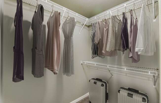 a closet with clothes hanging on a rack and luggage on the floor