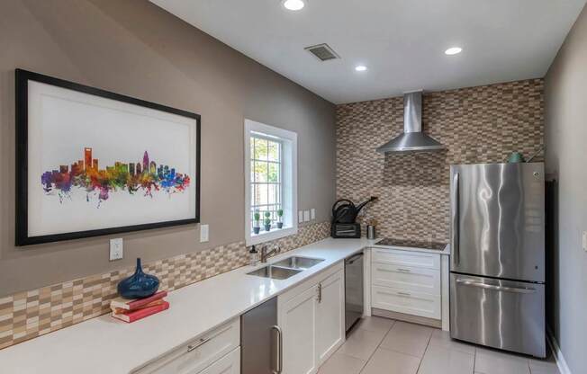 A kitchen with a stainless steel refrigerator and a cityscape picture on the wall.