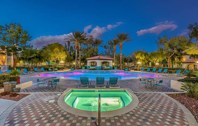 a large swimming pool with chairs and a jacuzzi at night at Mirasol Apartments, Las Vegas, NV