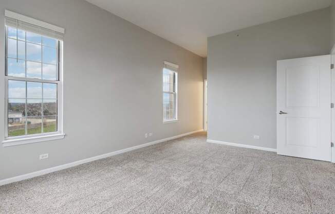 A room with a carpeted floor and two windows.
