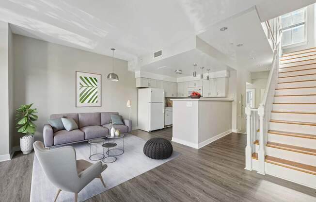 A living room with a grey sofa and a white kitchen in the background.