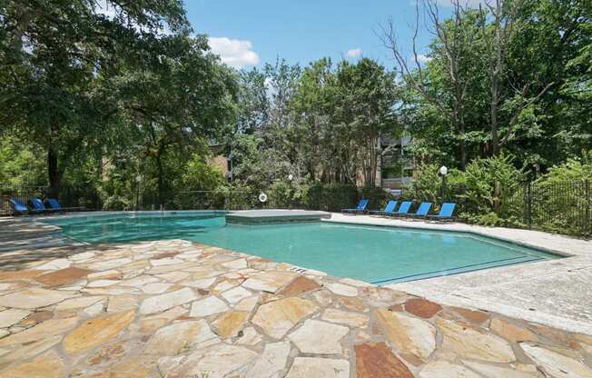 a swimming pool with blue chairs around it and trees in the background