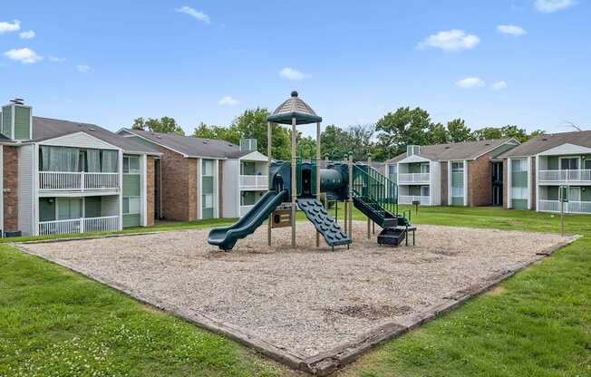 A playground with a green slide in the middle of a sandy area.