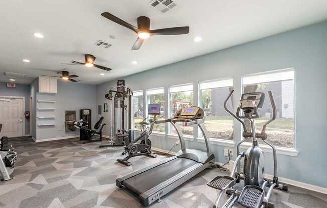 A spacious gym with treadmills, elliptical machines, and a fan.
