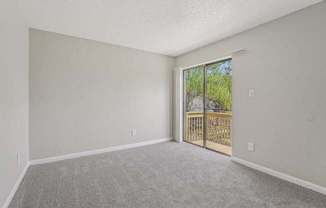 A room with a carpeted floor and a sliding glass door leading to a balcony.