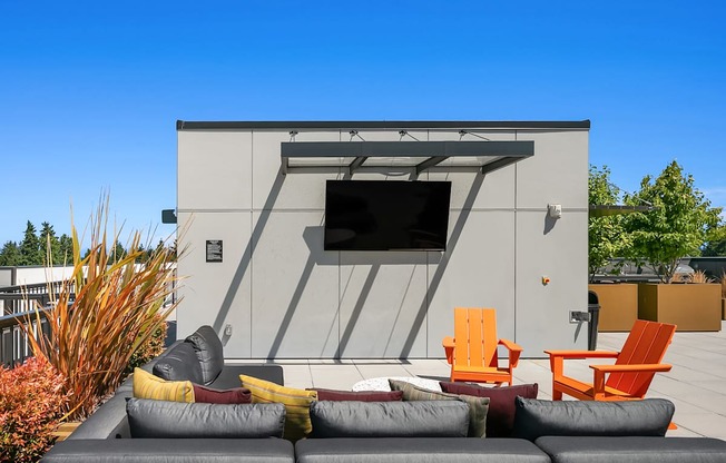 A modern outdoor seating area with a grey couch, orange chairs, and a grey sofa.
