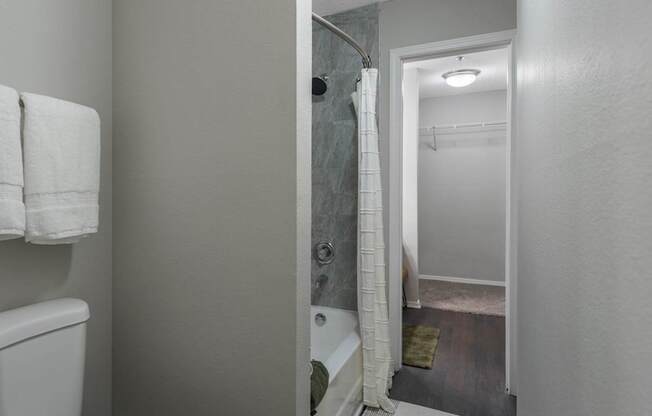 A bathroom with a toilet, a shower curtain, and a doorway leading to another room.
