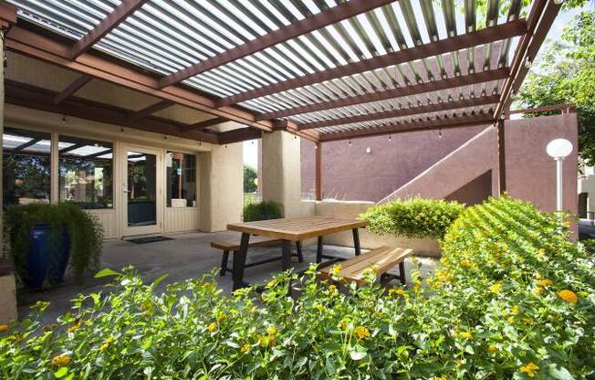 A patio with a wooden table surrounded by green plants.