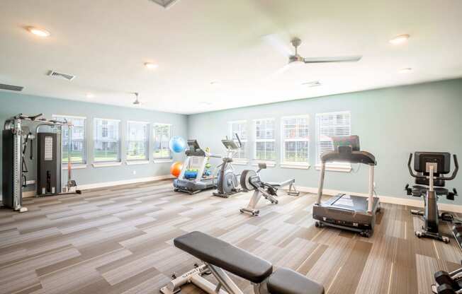 Fitness room with treadmills a bench and elliptical at Trillium apartments in Melbourne fl