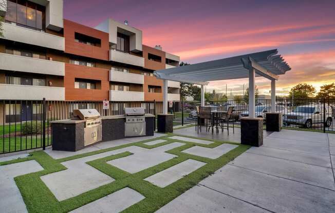 a patio with a grill and a building with a sunset in the background