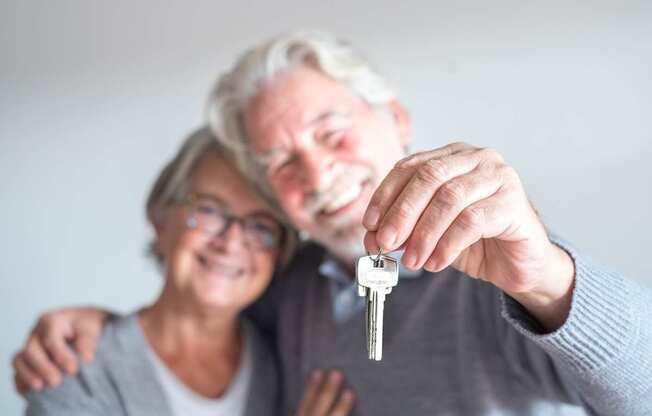 An elderly couple is holding a key together.