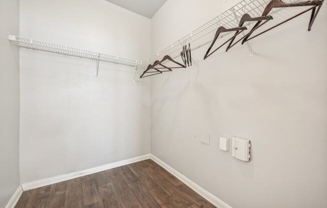 an empty room with white walls and wood flooring and a white closet with hooks